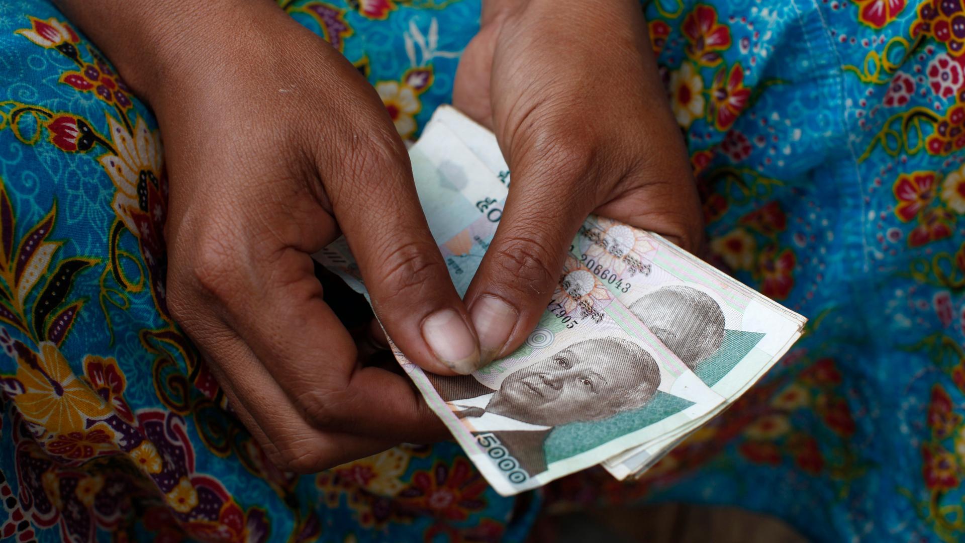 Weibliche Hände mit dunkler Hautfarbe halten ein Bündel kambodschanische Geldscheine