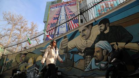 Eine Frau läuft vor einem Wandbild in Teheran entlang, das mit US-amerikanischen und israelischen Flaggen umwickelte Särge zeigt.