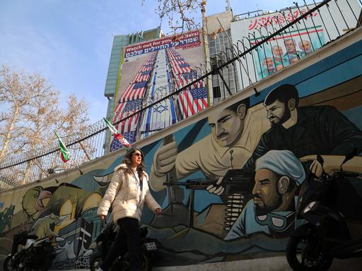 Eine Frau läuft vor einem Wandbild in Teheran entlang, das mit US-amerikanischen und israelischen Flaggen umwickelte Särge zeigt.