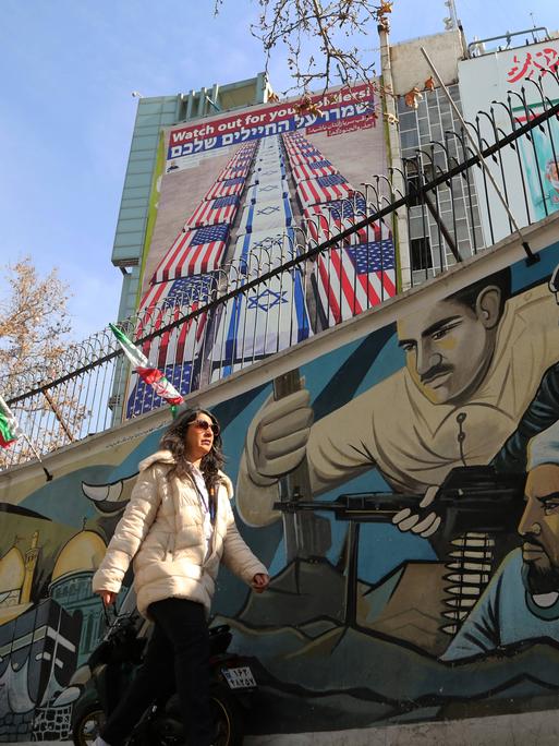 Eine Frau läuft vor einem Wandbild in Teheran entlang, das mit US-amerikanischen und israelischen Flaggen umwickelte Särge zeigt.