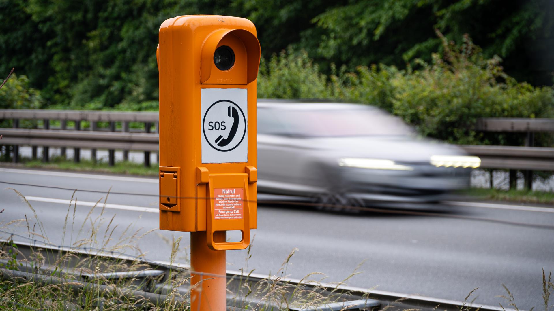 Eine Notrufsäule an der Autobahn mit vorbeifahrendem Verkehr.