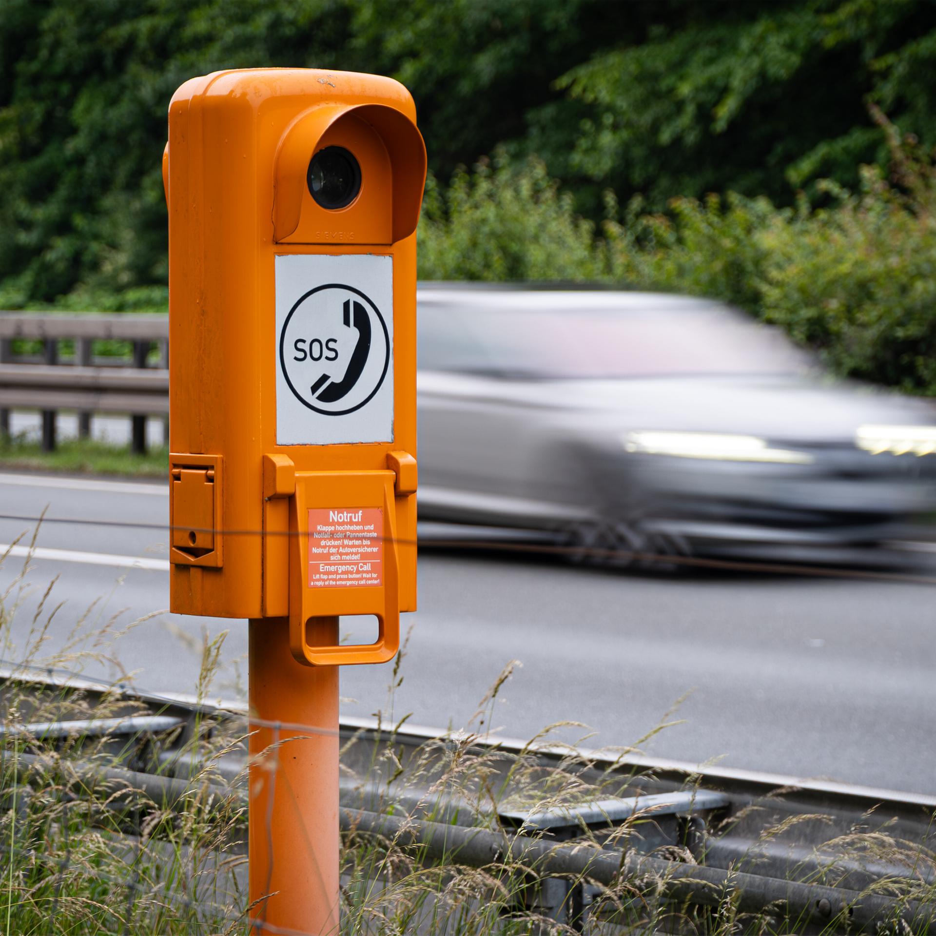 Eine Notrufsäule an der Autobahn mit vorbeifahrendem Verkehr