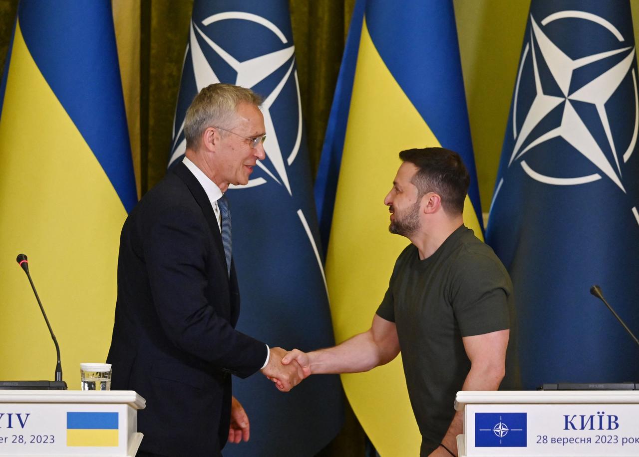 NATO-Generalsekretär Stoltenberg und der ukrainische Präsident Selenskyj geben sich die Hand. Hinter ihnen hängen Fahnen der NATO und der Ukraine.