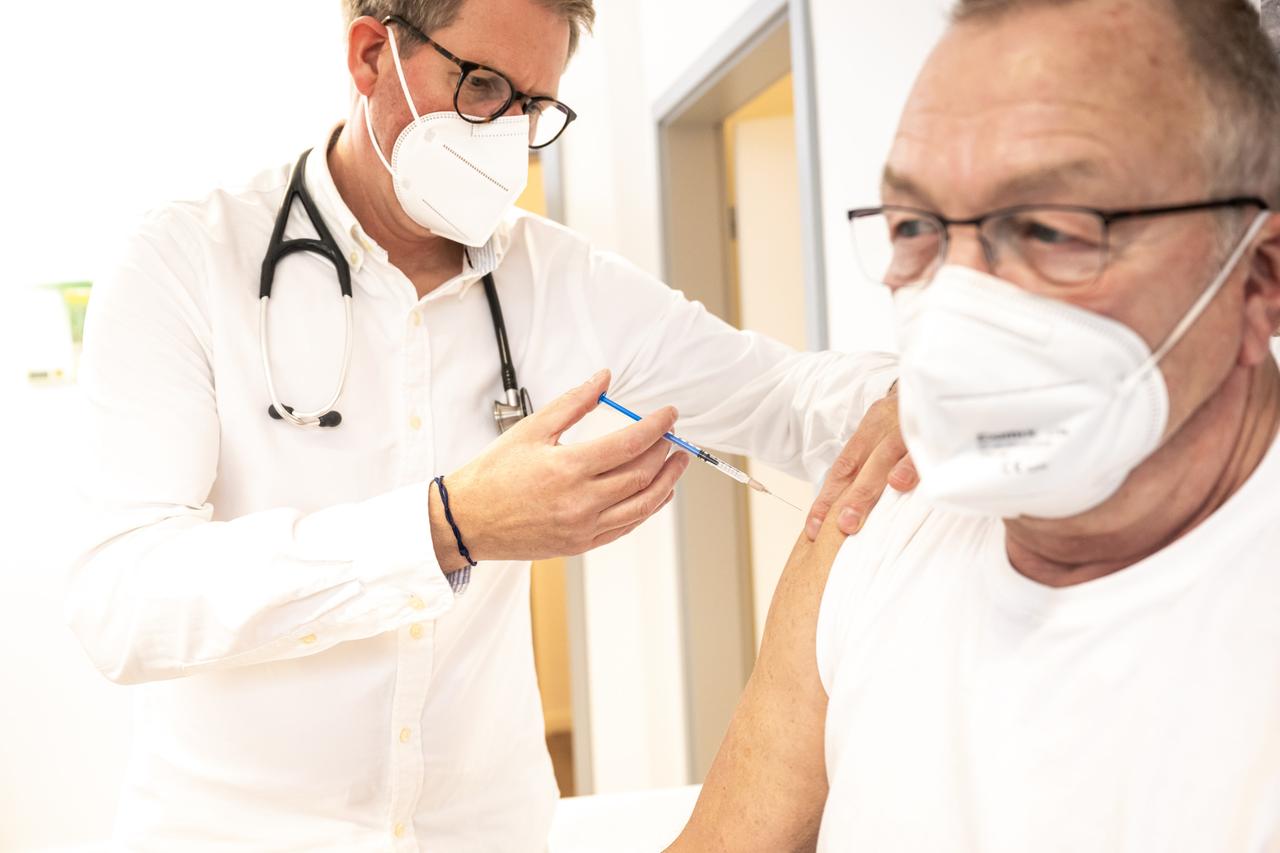 Ein Hausarzt verabreicht in einem Sprechzimmer seiner Praxis einem älteren Patienten eine Spritze (gestellte Szene)
