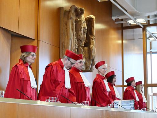 Mehrere Richter stehend in roter Robe. Hinter ihnen eine Wand mit einer steinernen Skulptur.