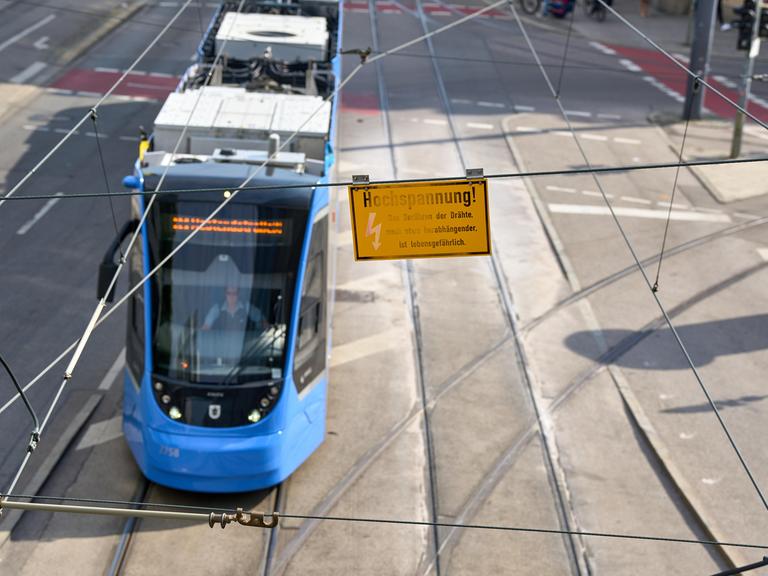 Eine Warnung vor Hochspannung hängt an der Oberleitung über einer vorbeifahrenden blauen Straßenbahn. (Symbolbild)