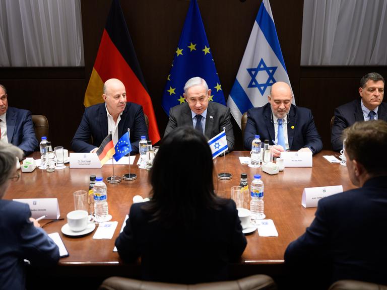 Bundesaußenministerin Annalena Baerbock (in der Mitte von hinten) sitzt zwischen ihren Beratern an einem Tisch gegenüber Israels Premierminnister Benjamin Netanjahu, neben den ebenfalls andere Männer sitzen. Im Hintergrundn sind die Fahnen (von links nach rechts) von Deutschland, der EU und Israels drapiert. 