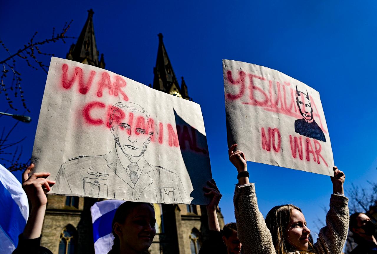 Zwei junge Frauen halten vor der Ludmila Kirche in Prag Plakate hoch, in denen Outin als Kriegsverbrecher bezeichnet wird. 