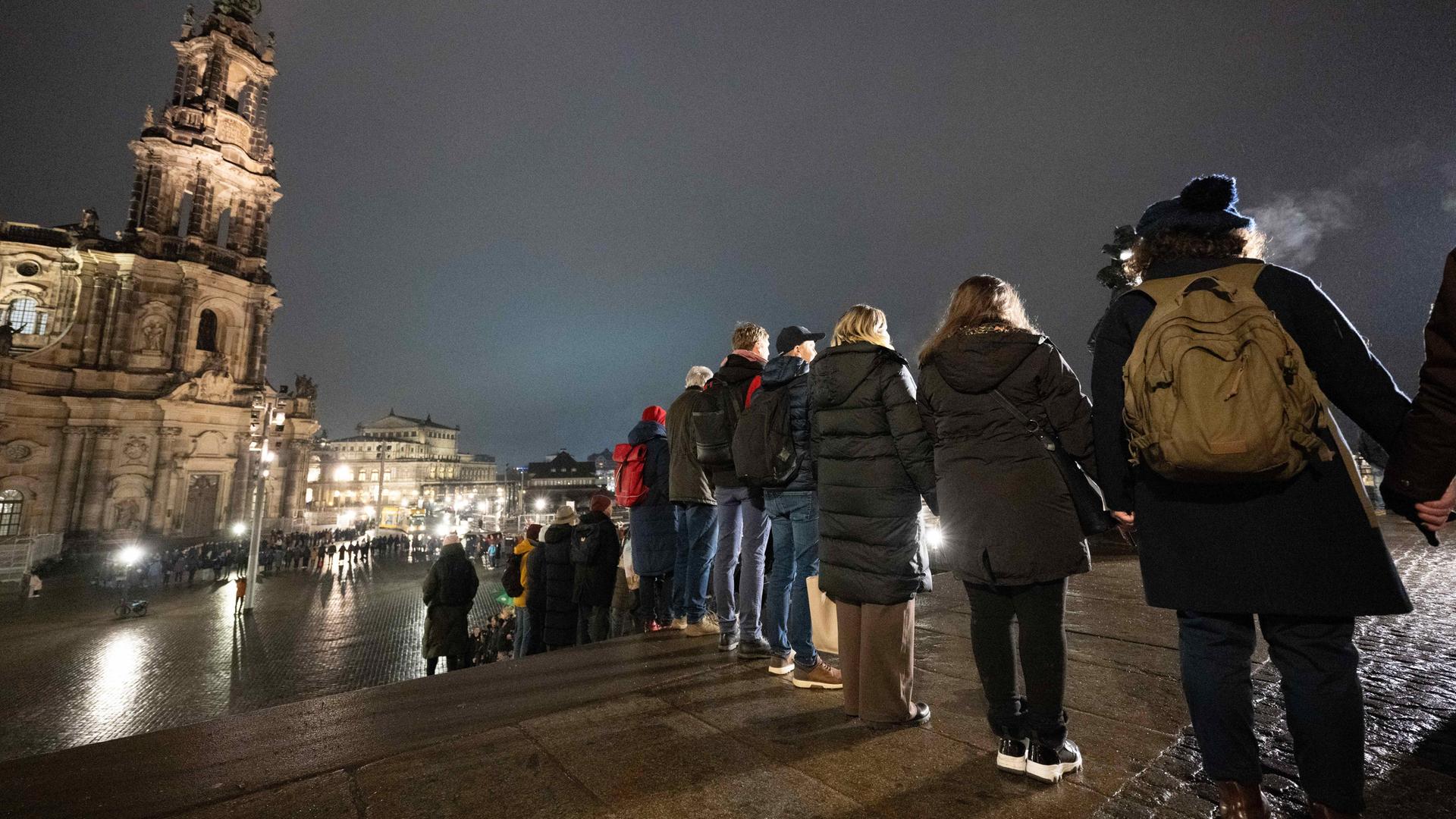 Zahlreiche Menschen stehen nebeneinander vor der Katholischen Hofkirche in Dresden und bilden eine Menschenkette. 