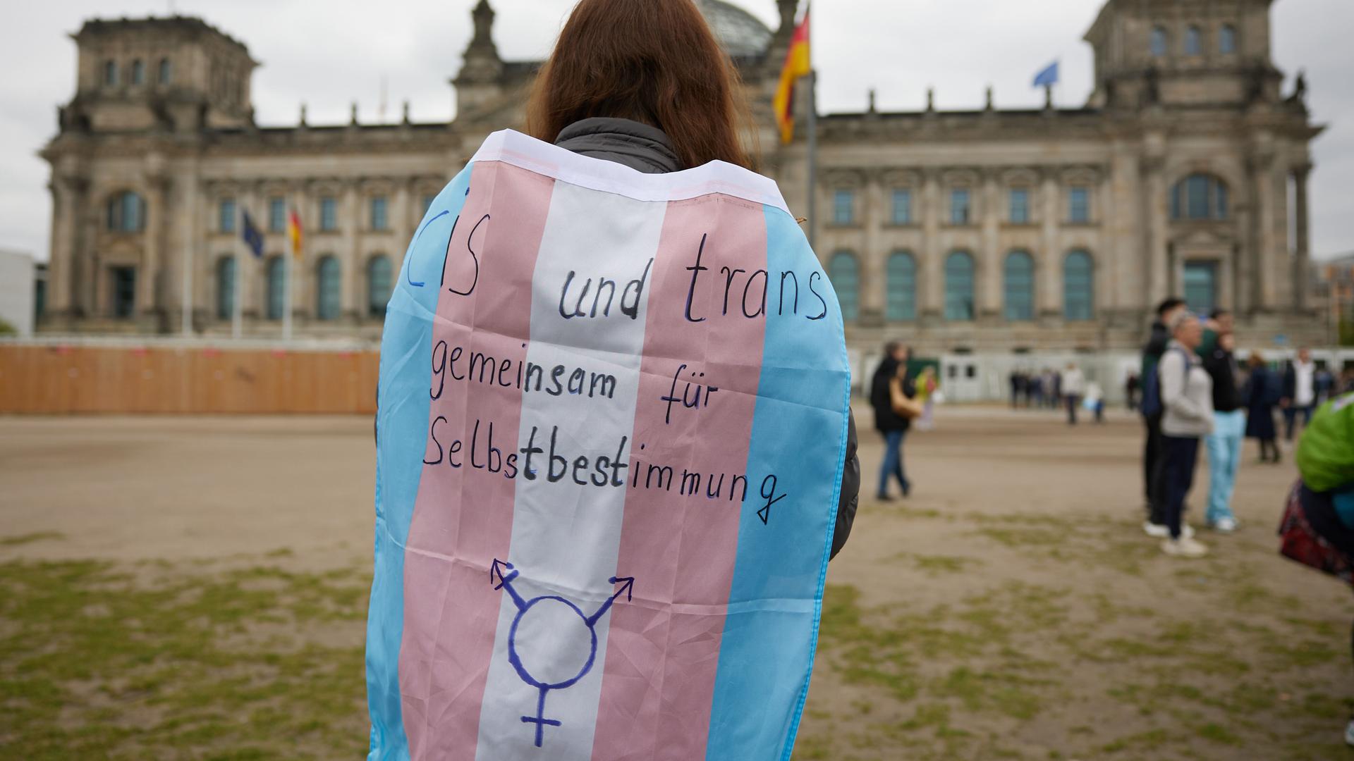 Eine Person steht mit einer Transgender-Pride-Flagge vor dem Bundestag.