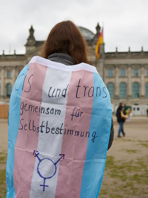 Eine Person steht mit einer Transgender-Pride-Flagge vor dem Bundestag.