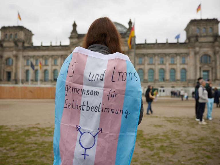 Eine Person steht mit einer Transgender-Pride-Flagge vor dem Bundestag.