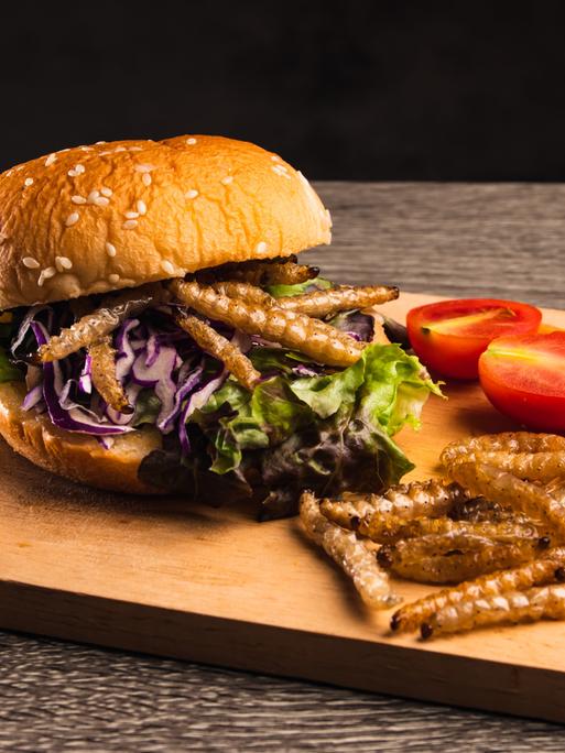 Hamburger mit gebratenen Bambusraupen und Gemüsesalat auf Holzteller.