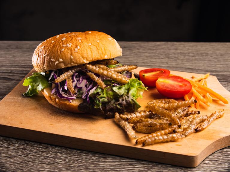 Hamburger mit gebratenen Bambusraupen und Gemüsesalat auf Holzteller.