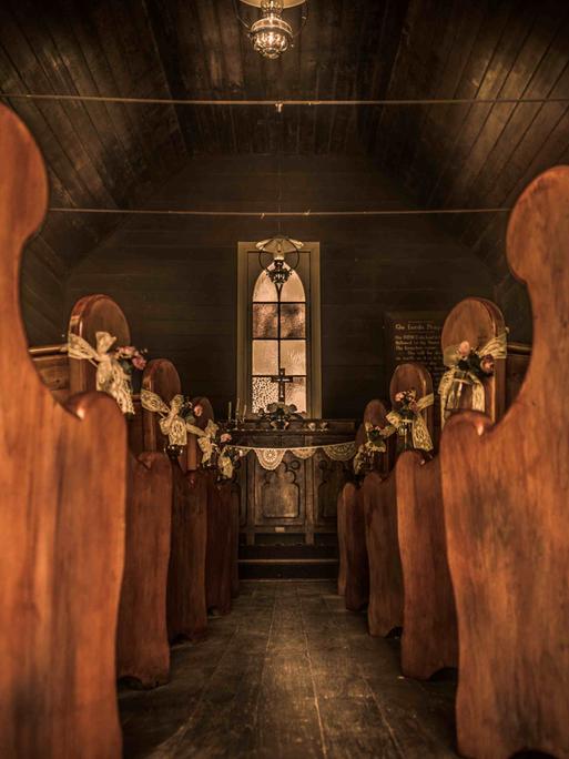 Blick entlang des leeren Gangs einer hölzernen Siedlerkirche zum Altar.