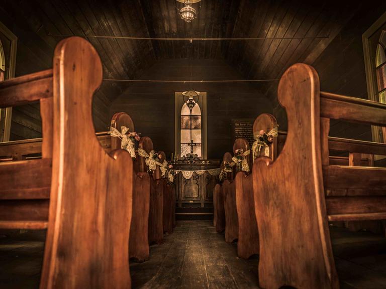Blick entlang des leeren Gangs einer hölzernen Siedlerkirche zum Altar.