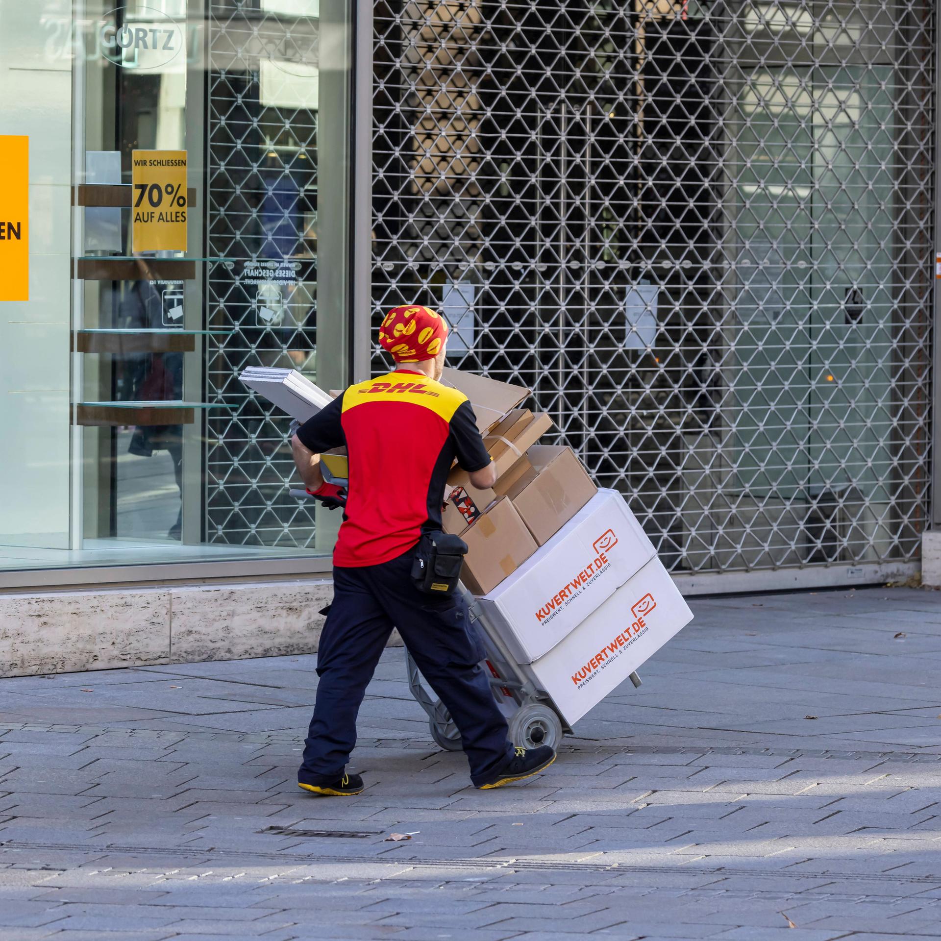 Ein Paketbote bugsiert viele Pakete auf einer Sackkarre durch die Innenstadt von Stuttgart. 