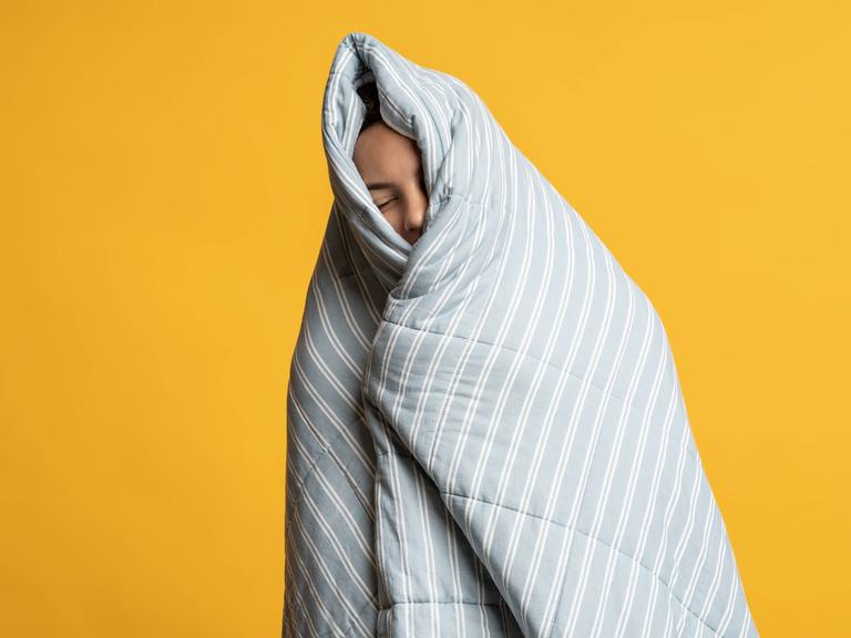 Aufwachvorgang in Bettdecke: ein eingemummelter Mensch mit geschlossenen Augen