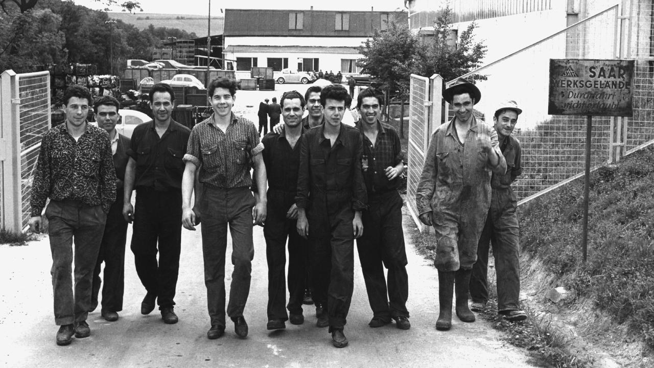 Historisches Schwarzweißfoto: Eine Gruppe spanischer Gastarbeiter verlässt das Werkgelände eines Betriebes.
