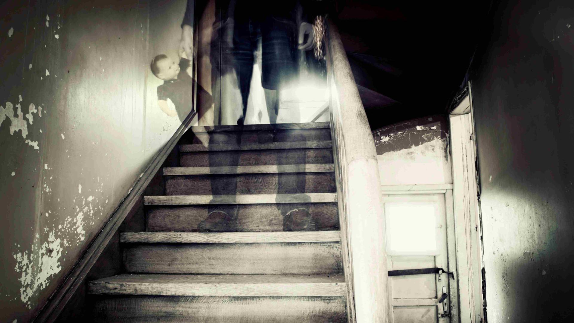 Eine Treppe in einem heruntergekommenen Haus, auf einer der Stufen steht die verschwommene, gespenstische Gestalt eines Mannes.