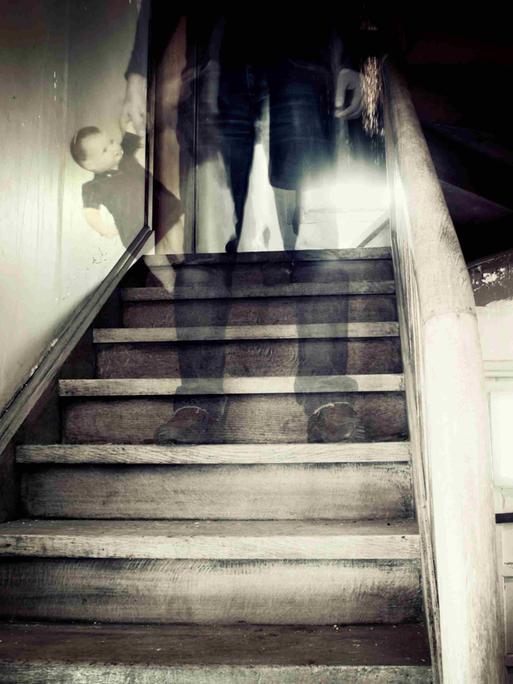 Eine Treppe in einem heruntergekommenen Haus, auf einer der Stufen steht die verschwommene, gespenstische Gestalt eines Mannes.