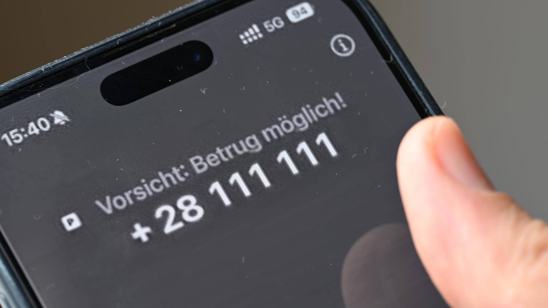 Ein Mann hält ein Smartphone, auf dem der Warntext "Vorsicht: Betrug möglich!" zu lesen ist. 