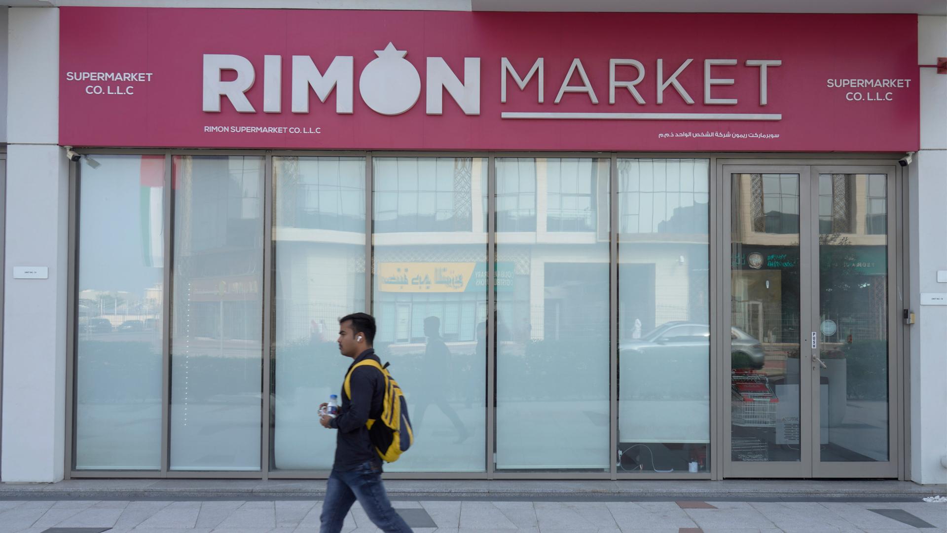 Ein Mann geht an einer Schaufensterfassade vorbei, über der "Rimon Market" steht. Die Fenster sind mit weißen Rollos verdeckt. 