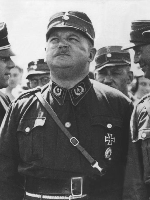 Ernst Röhm (M), Stabschef der SA (Sturmabteilung), in einer zeitgenössischen Aufnahme. Röhm trägt die Uniform der SA und blickt in den Himmel. Er ist umringt von anderen Mitgliedern der SA.