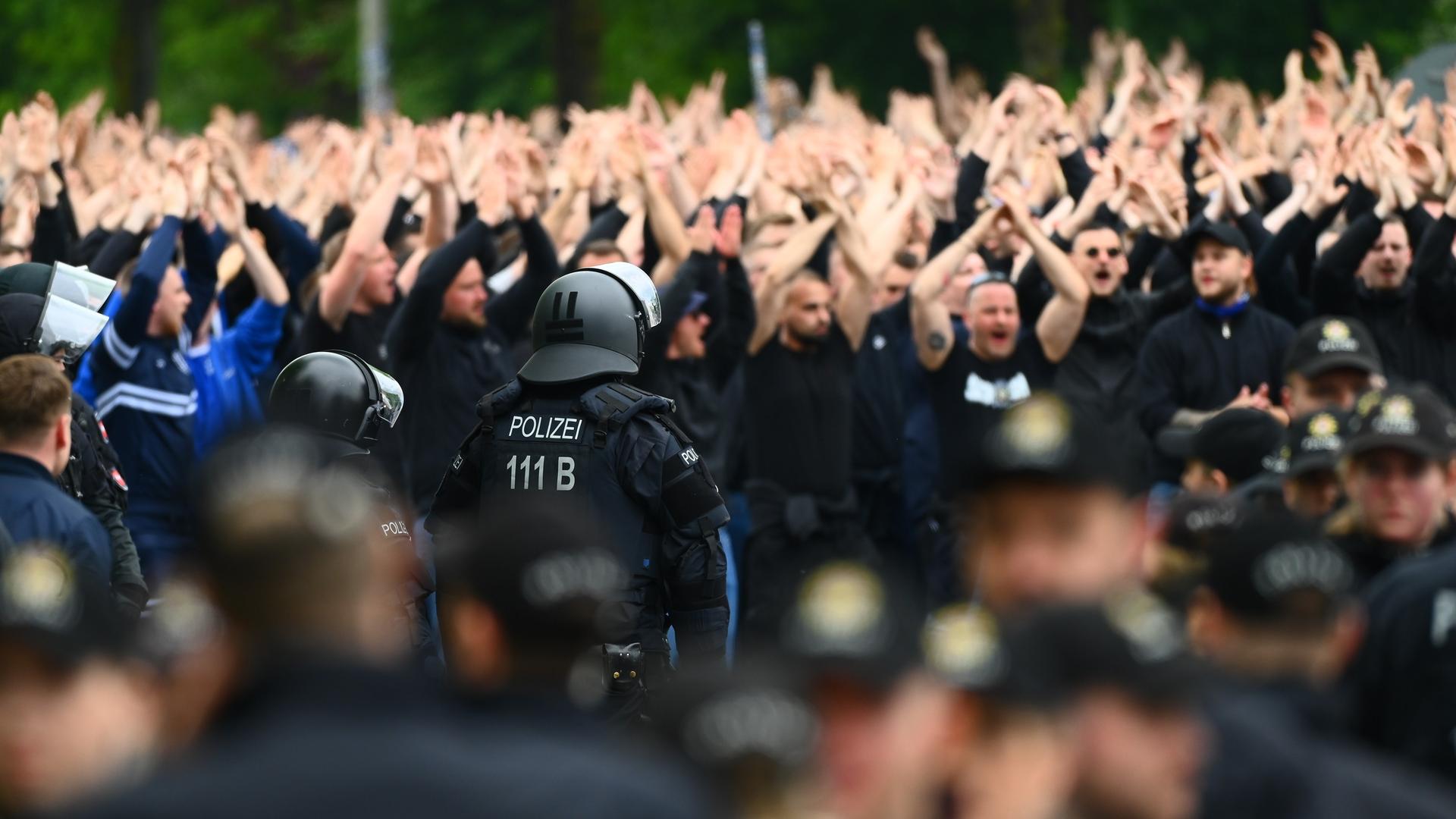 Polizisten sichern den Fanmarsch der HSV-Anhänger vor der Partie Hamburger SV - FC St. Pauli. Die Fans haben die Hände erhoben und rufen oder singen.