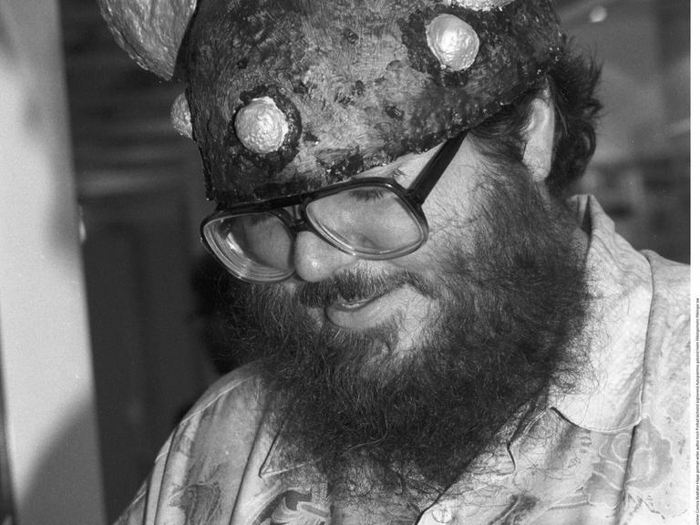 Schwarz-Weiß-Foto von Chris Browne, der einen Wikingerhelm trägt und einen Comicband von Hägar dem Schrecklichen signiert.