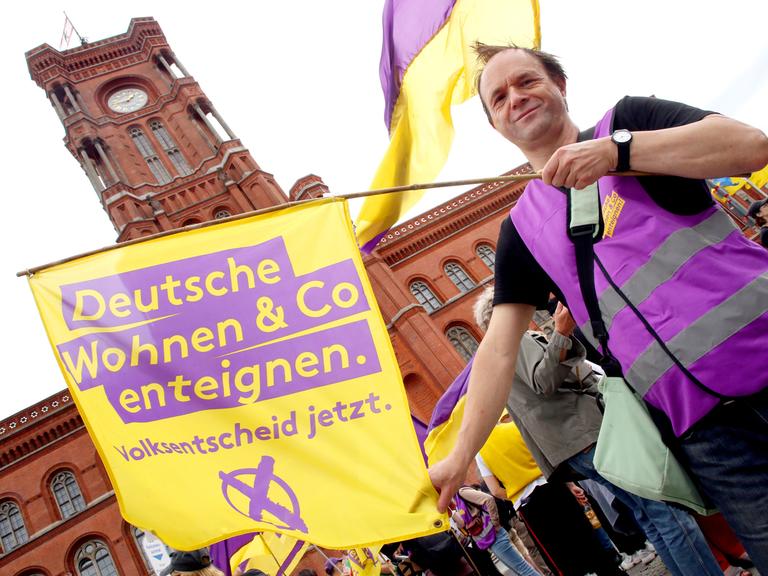 Ein Demonstrant hält eine Fahne mit der Aufschrift "Deutsche Wohnen & Co enteignen" während einer Kundgebung vor dem Roten Rathaus in Berlin.
