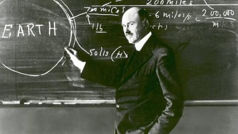 Auf dem Schwarz-weiß-Foto ist Robert Goddard an einer Kreidetafel zu sehen, auf der neben einem Kreis mit der Schrift "Earth" Berechnungen zu sehen sind
