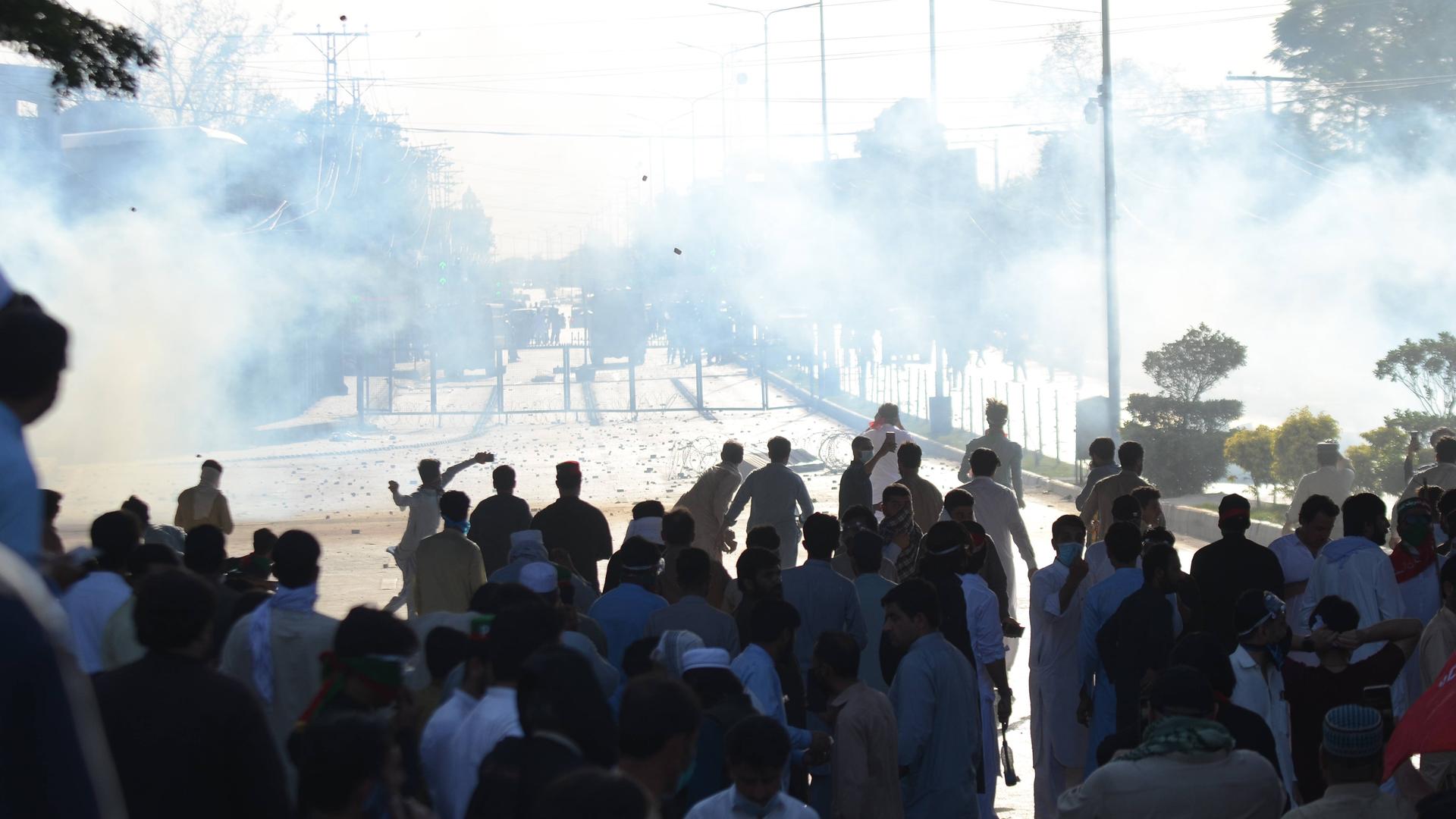 Auf einer Straße in der pakistanischen Stadt Peschawar demonstrieren viele Männer. Im Hintergrund sind Polizeifahrzeuge erkennbar, Tränengas wurde eingesetzt.