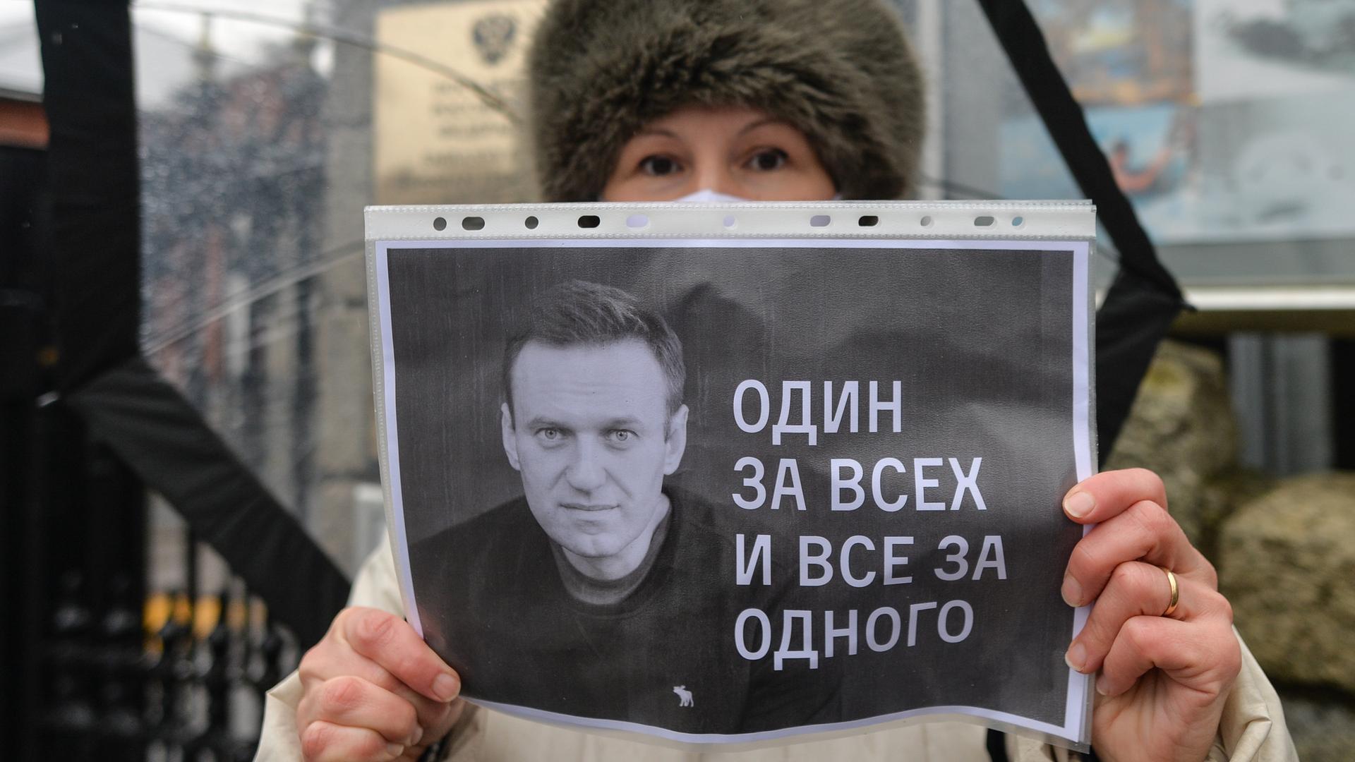 Eine Frau mit Pelzmütze hält eine schwarz-weiß-Kopie vor ihr Gesicht, auf dem Nawalny zu eine Reihe von Zahlen und Buchstaben zu sehen sind.