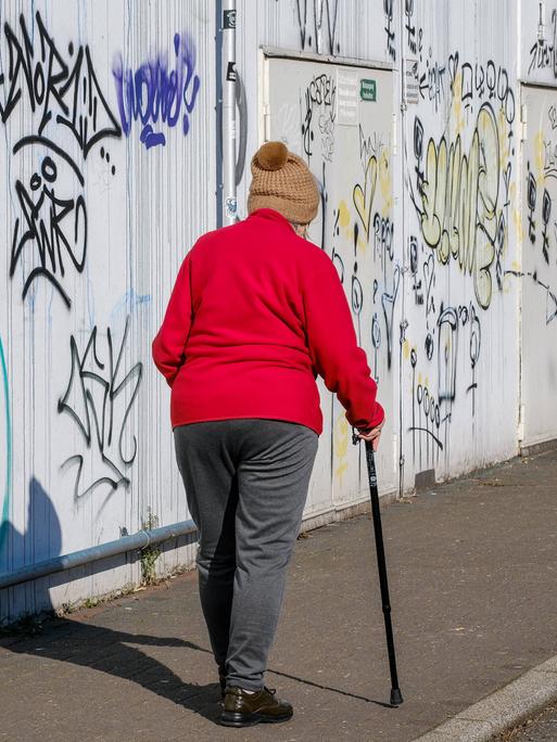 Alter Mensch mit Stock vor einer Graffiti-Wand 