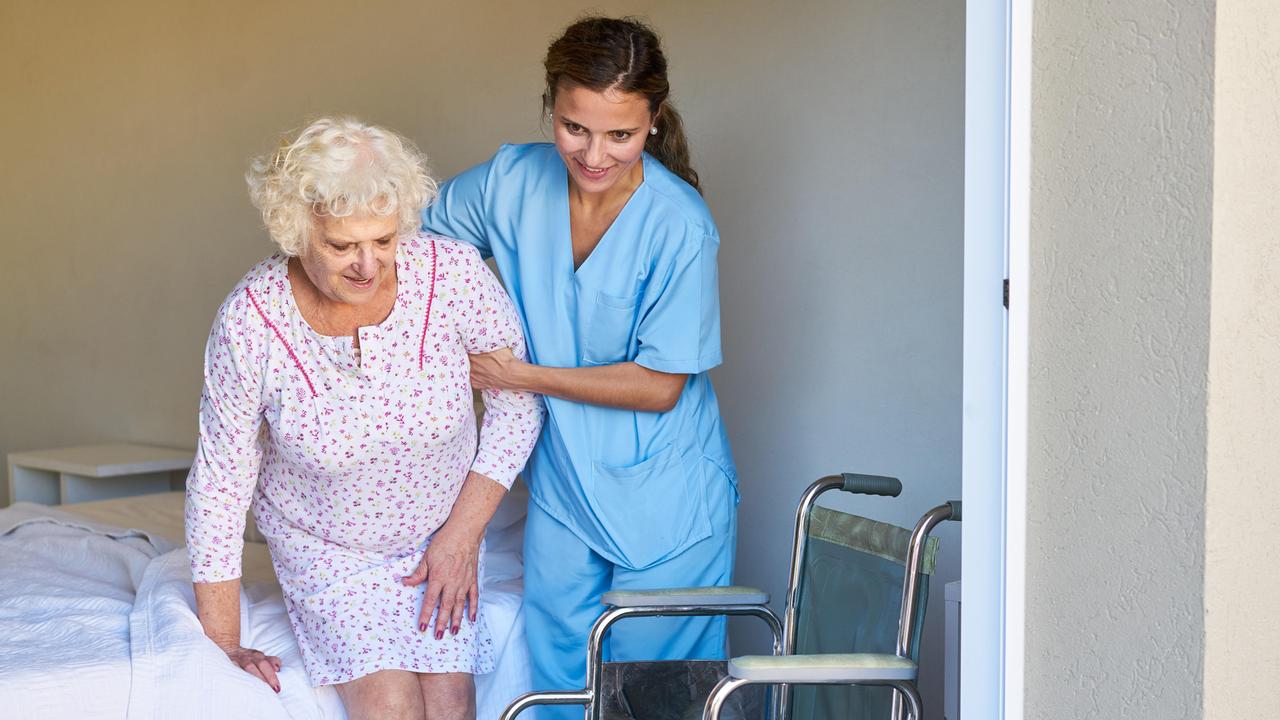Eine Altenpflegerin hilft einer Seniorin im Bett beim Aufstehen