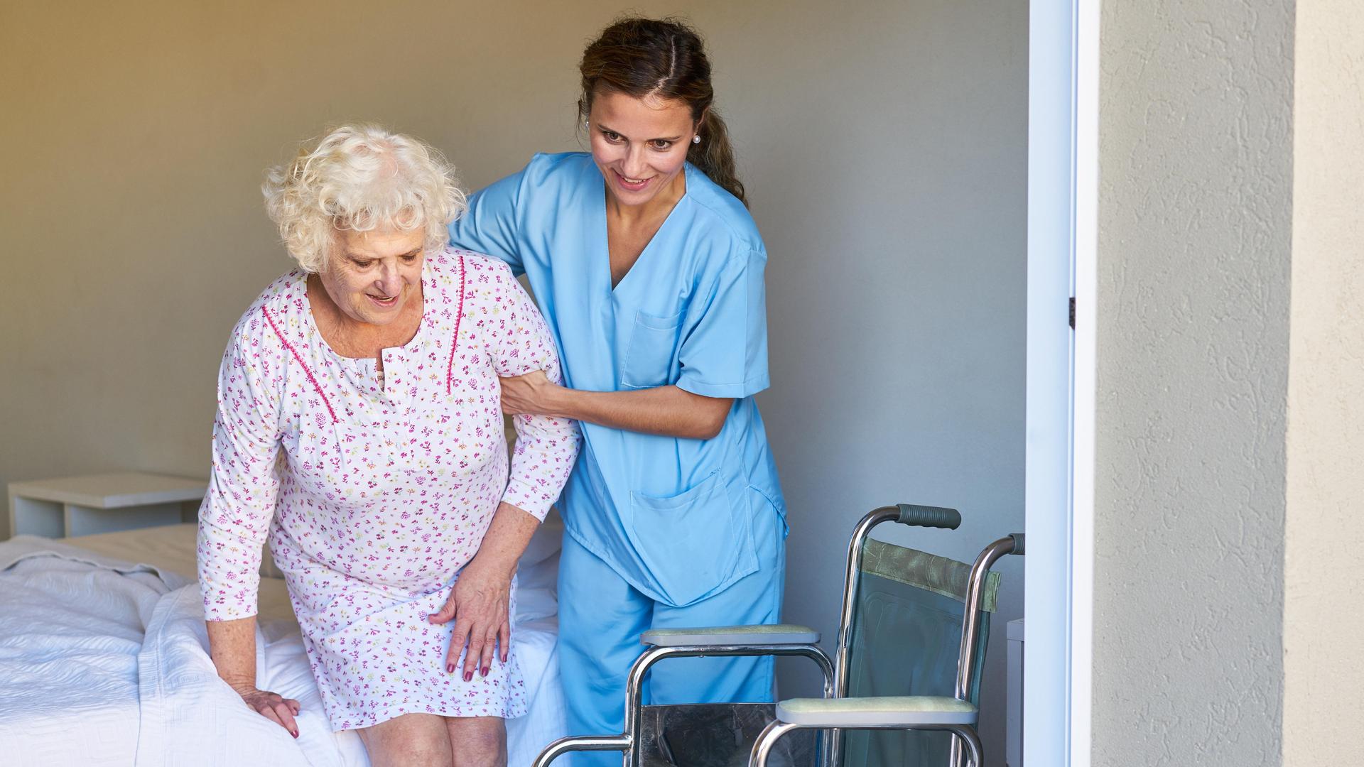 Eine Altenpflegerin hilft einer Seniorin im Bett beim Aufstehen