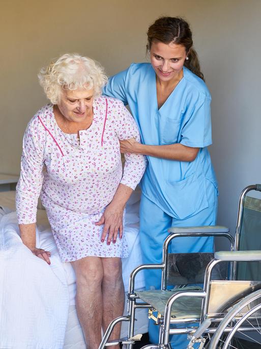 Eine Altenpflegerin hilft einer Seniorin im Bett beim Aufstehen