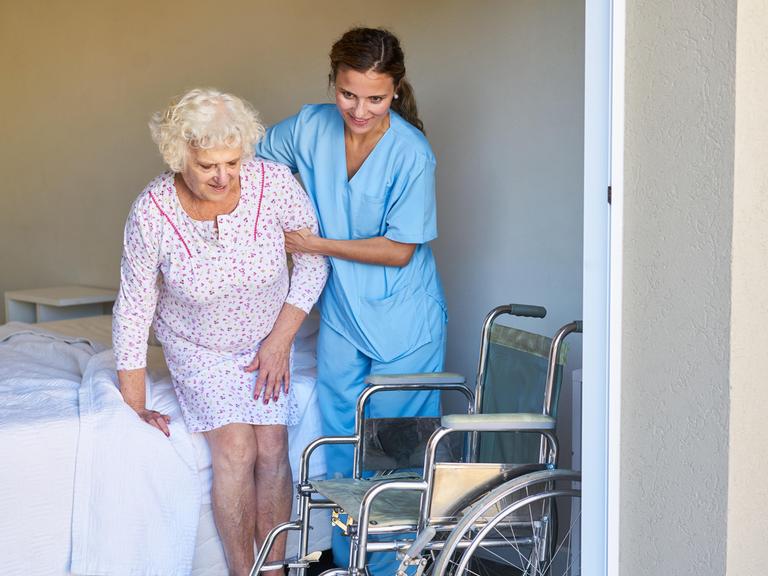 Eine Altenpflegerin hilft einer Seniorin im Bett beim Aufstehen