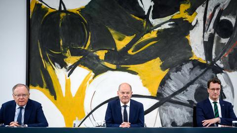 Stephan Weil, Olaf Scholz und Hendrik Wüst sitzen nebeneinander an einem Tisch. An der Wand hinter ihnen hängt ein großes modernes Gemälde.