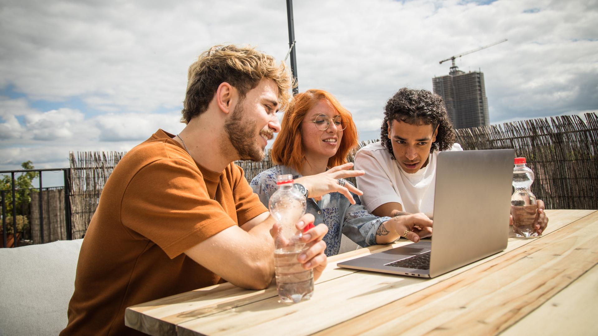 Eine Gruppe von jungen Leuten sitzt auf einer Dachterrasse in Berlin vor einem Laptop.