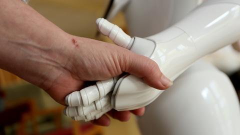 Eine menschliche Hand umfasst die Hand eines Roboters.