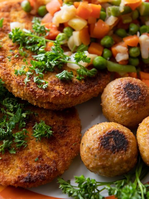 Vegane Falafel, vegane Schnitzel und Gemüse liegen auf einem Teller.