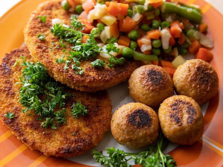 Vegane Falafel, vegane Schnitzel und Gemüse liegen auf einem Teller.