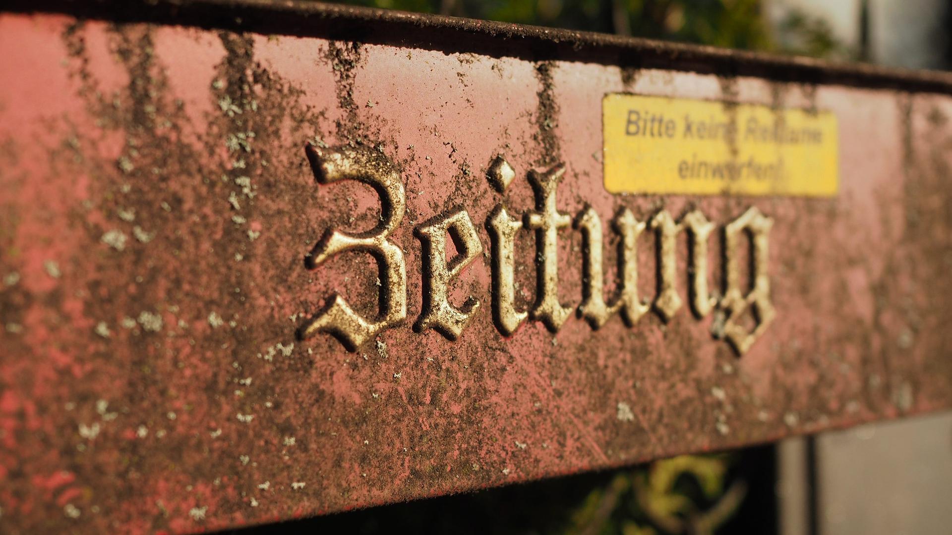 "Zeitung" steht in verwitterten Buchstaben auf einem Zeitungsbriefkasten an einem Haus.