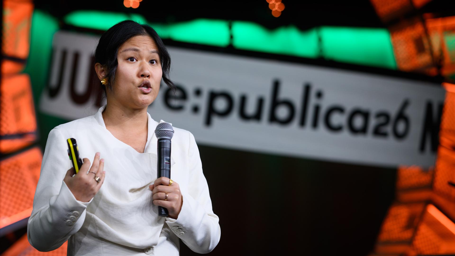 Karen Hao spricht vor einer bunten Digitalwand in ein Mikrofon. 