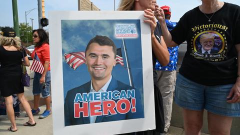 Eine Frau trägt ein Plakat mit dem Bild von Charlie Kirk, auf dem eine amerikanische Flagge zu sehen ist und die Worte "American Hero!" 
