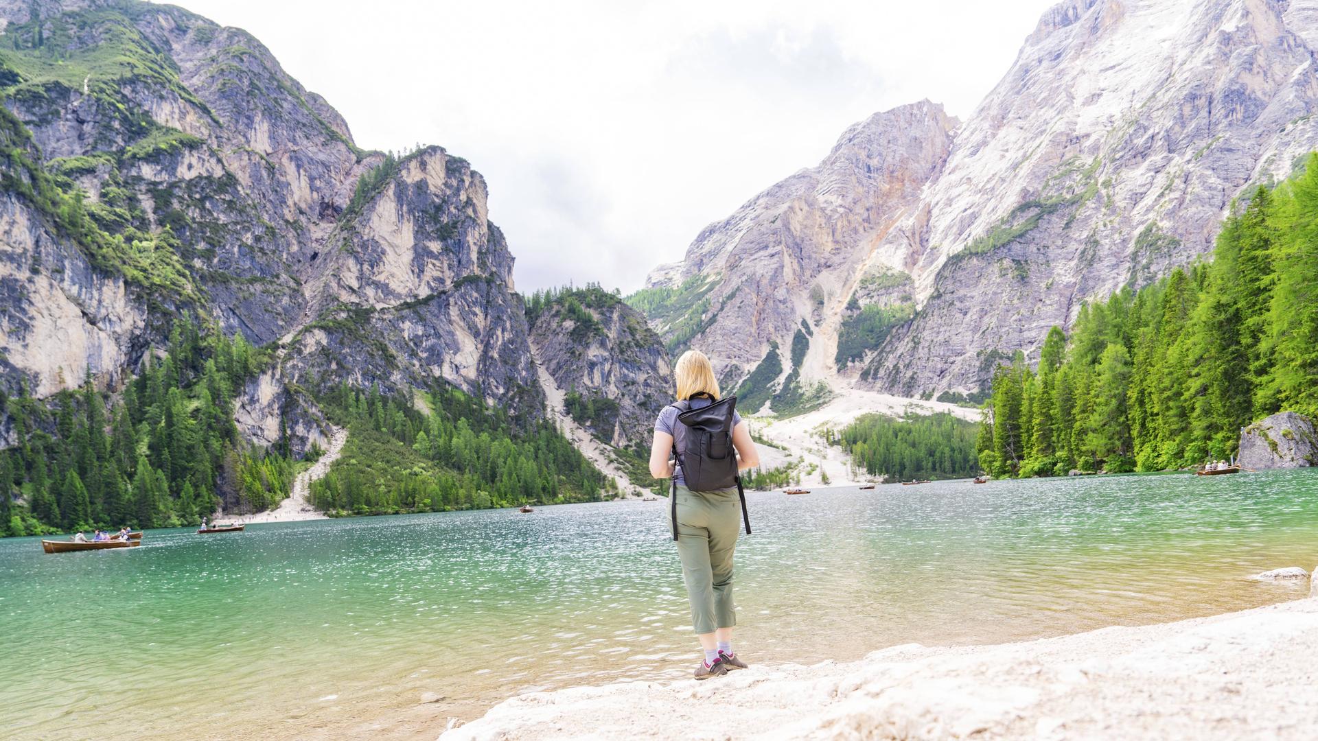 Eine Frau genießt die Aussicht von einem Seeufer auf die Dolomiten am Pragser Wildsee in Südtirol Eine Frau genießt die Aussicht von einem Seeufer auf die Dolomiten am Pragser Wildsee in Südtirol