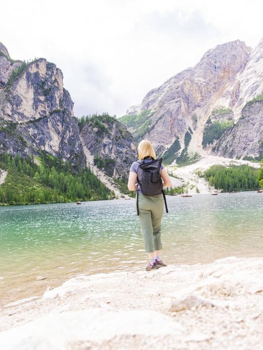 Eine Frau genießt die Aussicht von einem Seeufer auf die Dolomiten am Pragser Wildsee in Südtirol