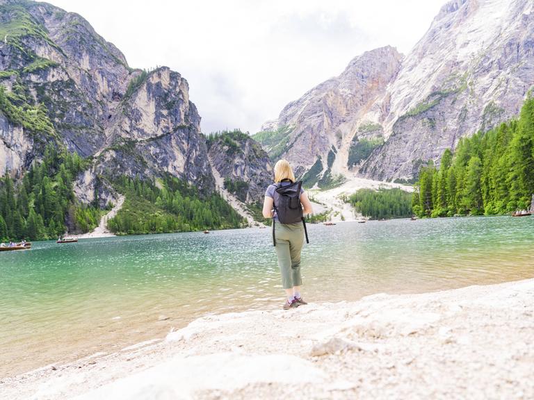 Eine Frau genießt die Aussicht von einem Seeufer auf die Dolomiten am Pragser Wildsee in Südtirol